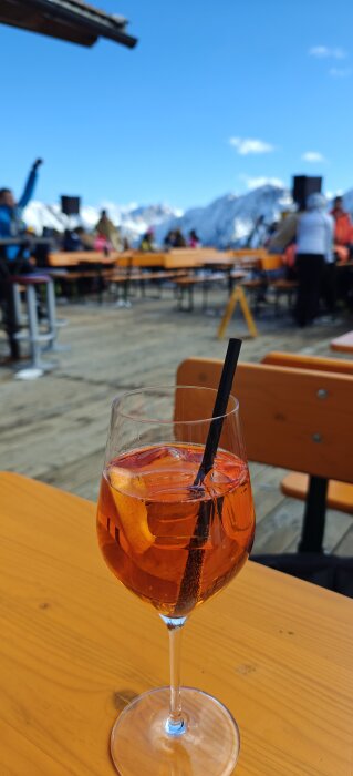 Aperol Spritz med is och apelsinskiva i vinglas på träbord utomhus med snöiga berg i bakgrunden.