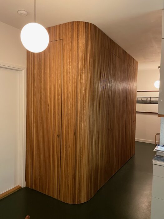 Nätt träpanelvägg med rundat hörn och dolda dörrar, byggd av reglar och ribbor för ett stilrent utseende.