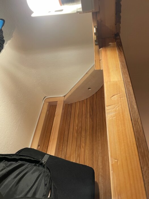 Inredning med träpanel och reglar, visar installationsdetaljer med gångjärn och rundning vid hörnet. En del av ett byggprojekt med fokus på stabilitet.