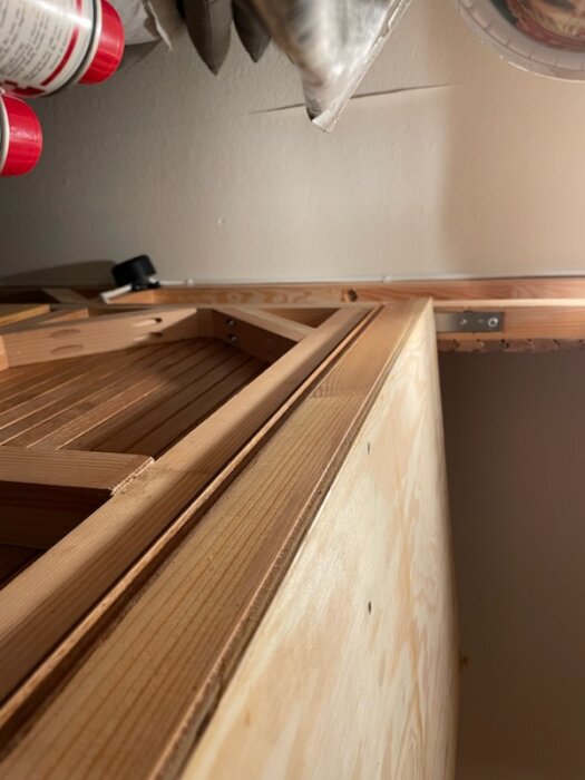 Träkonstruktion med reglar och ribbor, fastskruvade för stabilitet. Dörr med vridgångjärn i närbild. Verktygshylla synlig ovanför.