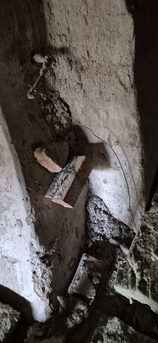 Spjäll uppe på vinden med vajer, monterat i murstocken, omgivet av grönt snöre och tegel, del av ventilationssystem som diskuteras i inlägget.