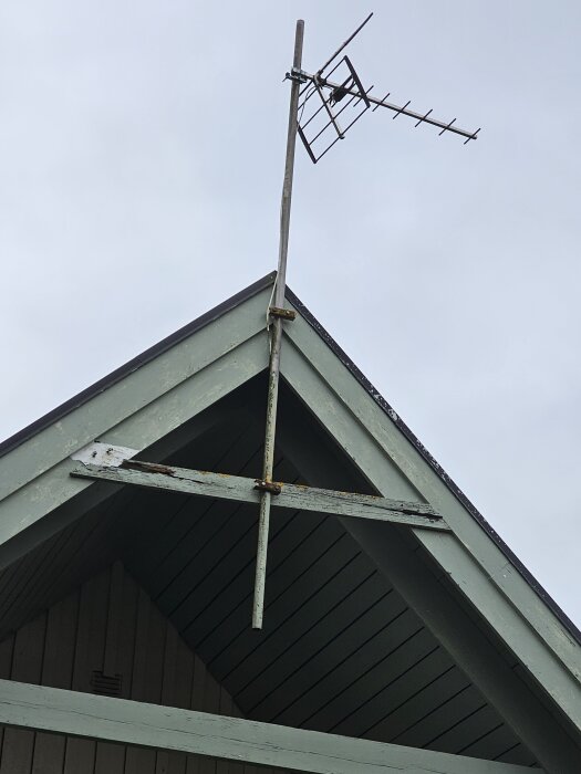 TV-antenn monterad på ett ruttnande bräde på ett husgavelns topp. Sladd från antennen går in i väggen.