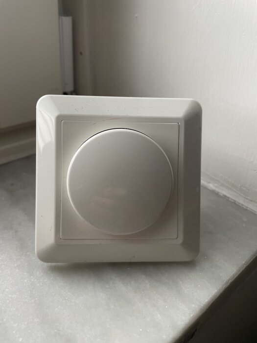 A white dimmer switch on a windowsill.