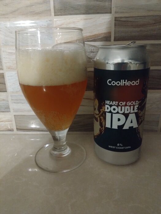 Ett glas med öl bredvid en burk märkt "CoolHead Double IPA", placerad på ett kaklat underlag.