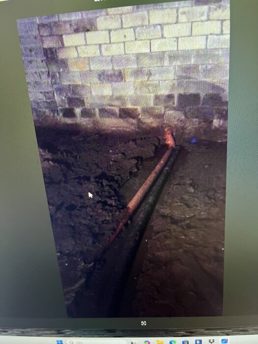 Panoramabild av en källare med synliga dräneringsrör och jordnära en tegelvägg, där vatten tränger in längs golvet.