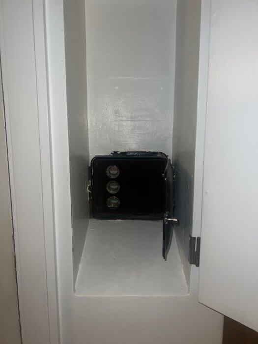 Gammal elcentral monterad i ett vitt skåp med öppen dörr, synligt inuti elcentralens fack för kablar och säkringar.