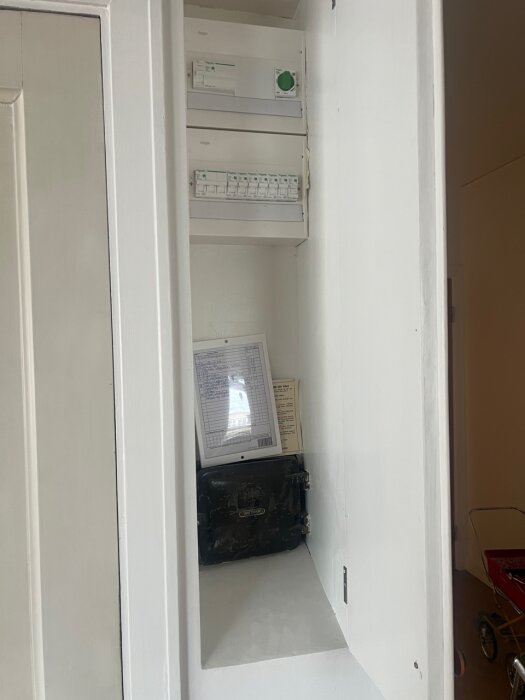 Gammal elcentral inuti ett skåp med en svart kabel, dokument och äldre utrustning synliga.