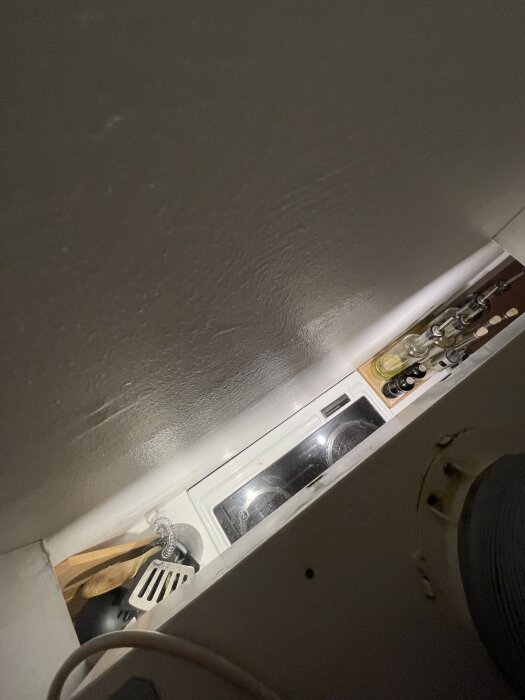 Mellanrum mellan köksfläkt och vägg med redskap och kryddor i bakgrunden.