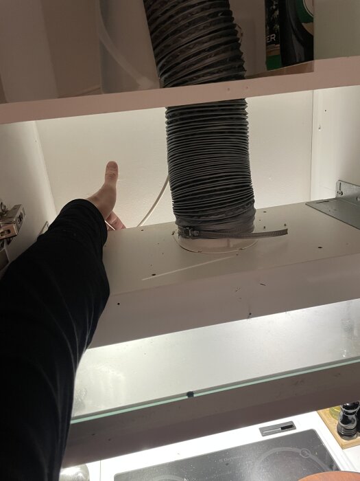 En hand mäter mellanrum mellan en köksfläkts böjliga slang och väggen ovanför en spis.