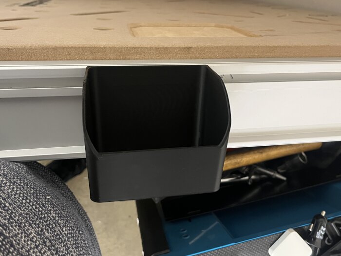 Svart 3D-utskriven låda monterad i skena på workbench, användbar för förvaring av verktyg och tillbehör.