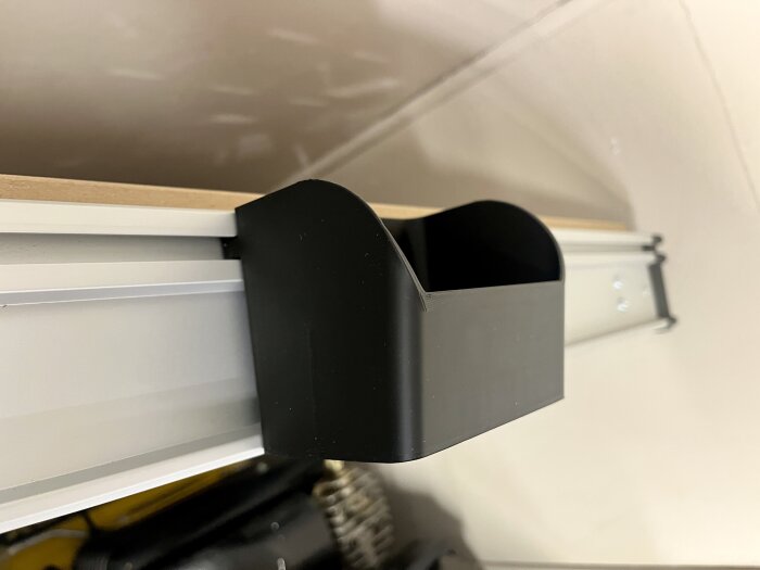 Svart 3D-utskriven låda monterad på en skena för verktygsförvaring i en verkstadsmiljö.