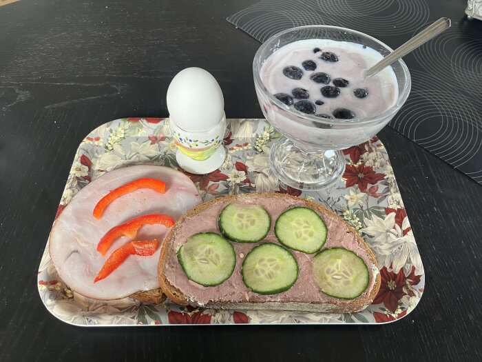 Frukost på bricka: mackor med kalkon, paprika, leverpastej och gurka, kokt ägg och yoghurt med blåbär i en skål.