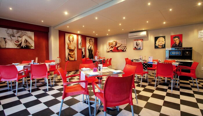 Matsal med schackrutigt golv, röda stolar och konstverk på väggarna.