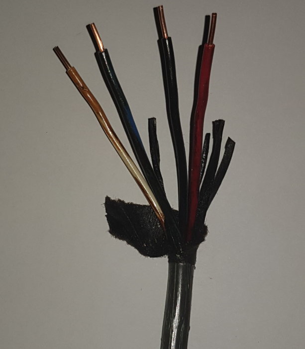 Exponerad kabel med flera färgade kopparledare och svart isolering, möjliga EKR eller äldre kulokabel, med pappers- och PVC-isolering.