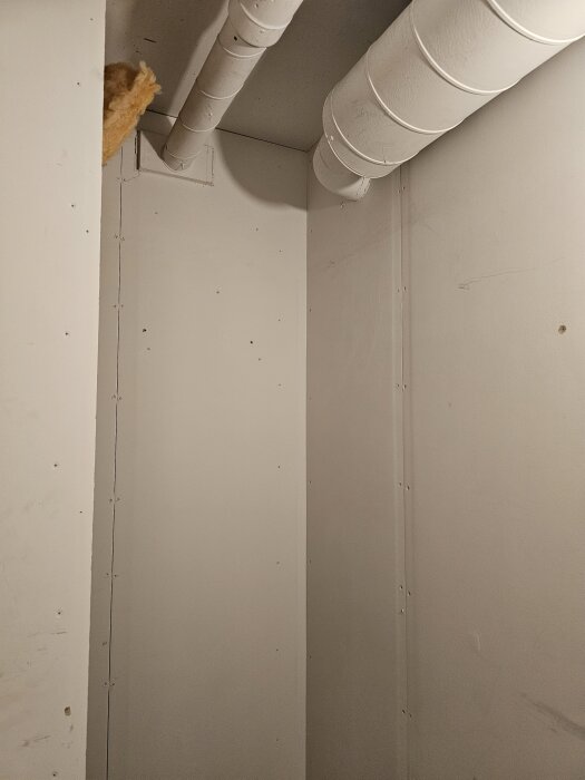 Vitmålat rum med takventilationsrör.