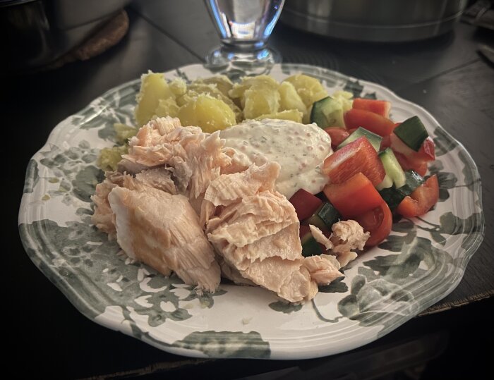 Ugnsbakad lax med potatis, sallad av gurka och paprika, toppad med romsås på en tallrik.