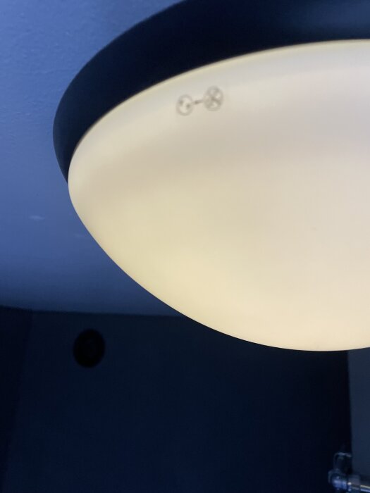 Rund vit kåpa på en taklampa mot blå bakgrund.