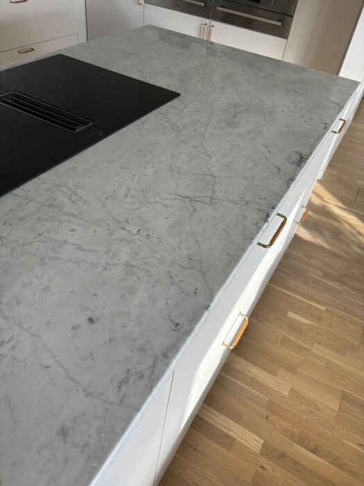 Carrara marmor bänkskiva i kök, med ljus träparkettgolv och induktionshäll.