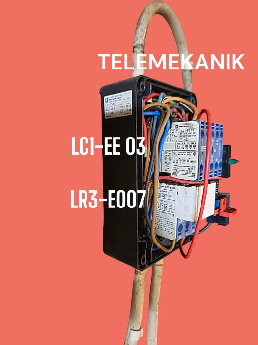 Elektrisk komponentbox märkt "TELEMEKANIK" med kablar, modellnummer LC1-EE 03 och LR3-E007 mot en röd bakgrund.