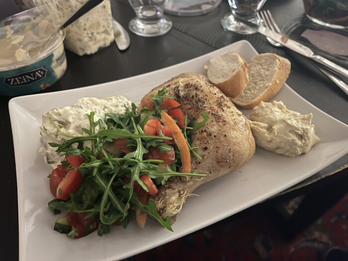 Tallrik med kyckling, sallad, potatissallad, hummus och två skivor bröd.
