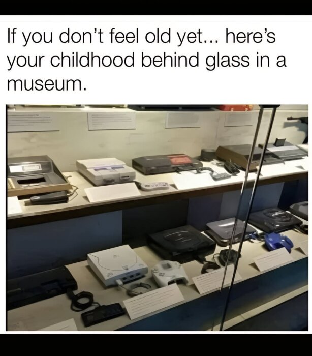 Vitrin med gamla spelkonsoler i museum, inklusive text om barndomsnostalgi.