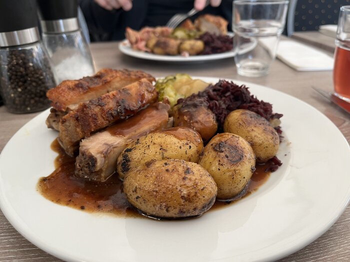 Tallrik med revben, potatis, sås, rödkål, inlagd gurka och äppelmos.