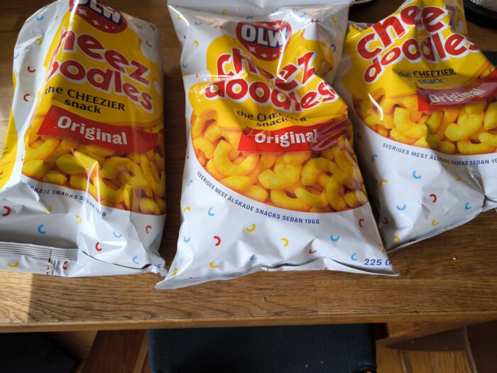 Tre påsar OLW Cheez Doodles original, 225 gram, på ett träbord.