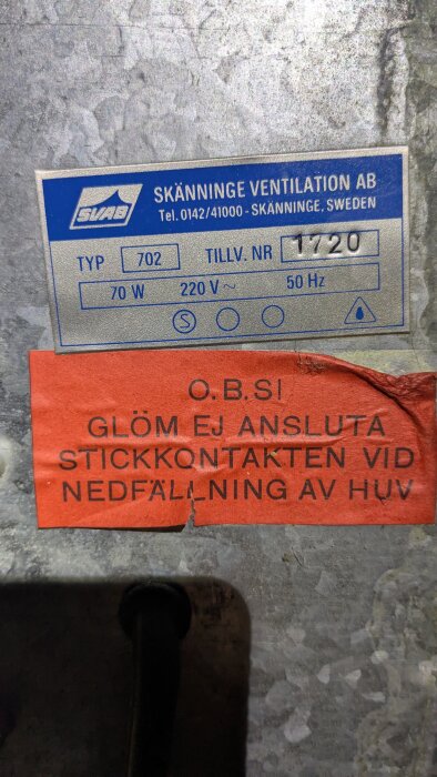 Etikett på ventilationsenhet från Skänninge Ventilation AB, modell 702, 70W, 220V, med varning om stickkontakt vid nedfällning av huv.