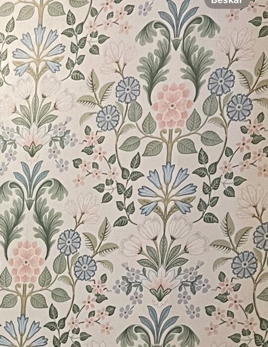 Närbild av en blomsterfärggrann tapet med mönster i pastellfärger, föreställande blommor och lövverk i grönskande nyanser.