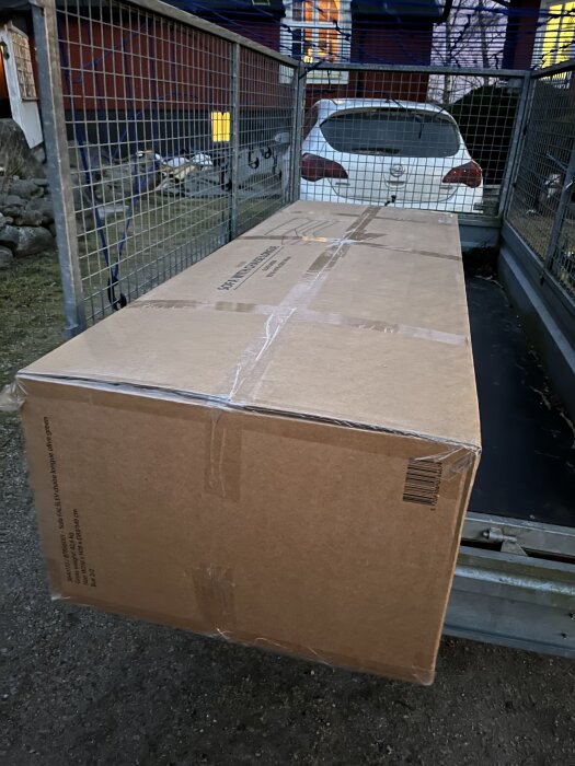 Stort paket på en släpvagn bakom en vit bil, redo för transport.