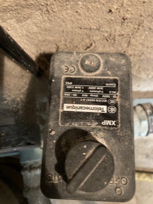 Bilden visar en dammig elektrisk brytare monterad på en vägg, med text och symboler synliga på framsidan.