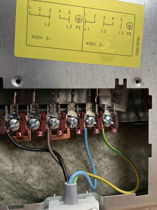 Kabelanslutningar i spisens kopplingsbox med numrerade skruvplintar och färgkodade ledningar: svart, brun, blå och grön/gul.