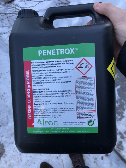 Behållare med desinfektionsmedel märkt "PENETROX" för sanering av mögel och lukt. Hålls av en hand, omgiven av snöig bakgrund.