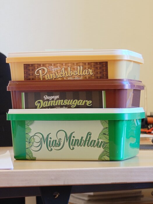 Tre plastlådor med godisnamn: Punschbollar, Dammsugare och Minthjärtan, staplade på ett bord.