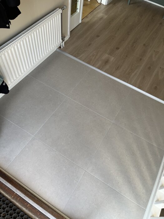 Grått klinkergolv intill en vit radiator och ljus träparkett i ett bostadsutrymme.