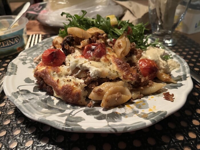 Köttfärsgratäng med pasta och mozzarella, toppad med tomater, serverad med sallad och bröd.