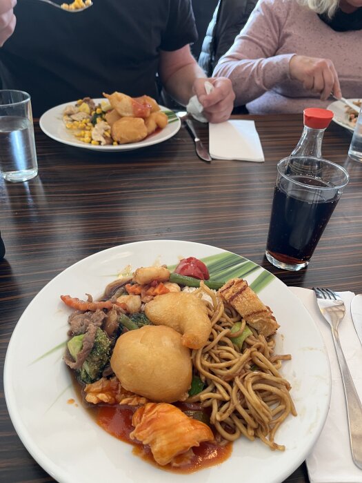 Två tallrikar med thaibuffé och dryck på ett matbord under en måltid med gäster.