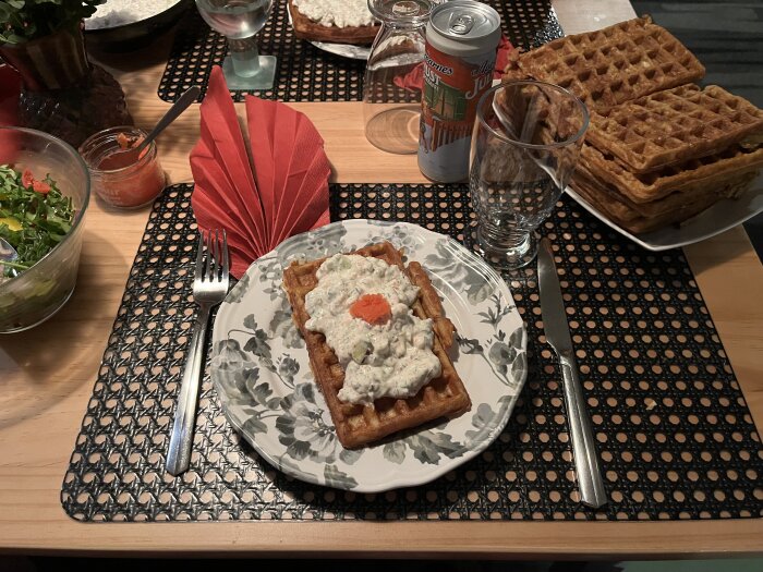 Belgisk potatisvåffla med räkröra och avokado på tallrik, serverad på dukat bord med våfflor, sallad och dryck i bakgrunden.