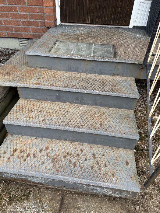 Rostiga metalltrappsteg framför en ytterdörr, med funderingar kring ommålning eller renovering.