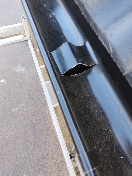 Öppning i svart hängränna som verkar märkligt klippt, med oro för att löv kan fastna. Synligt från byggnadsställning bredvid takets kant.