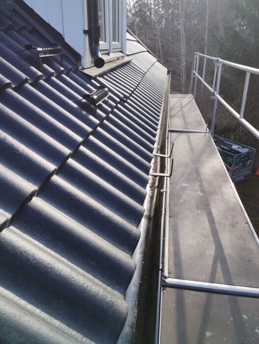 Tak med svarta takpannor och en hängränna. Synlig takkupa och byggställning. Fokus på takfotens och takpannornas skick.