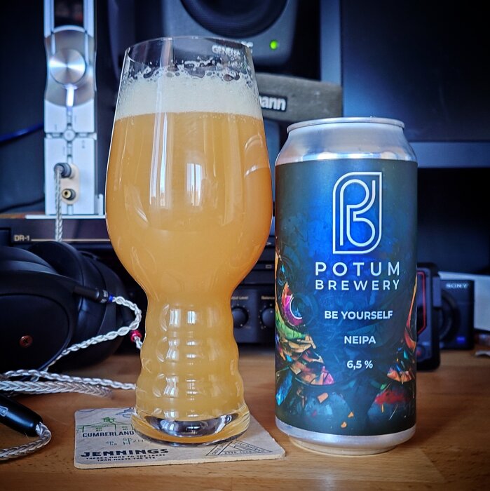 Ett glas med skummande NEIPA-öl bredvid en burk från Potum Brewery på ett bord.
