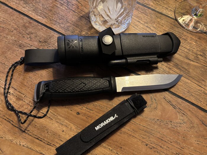 Rostfri Morakniv med svart handtag och slida på ett träbord.