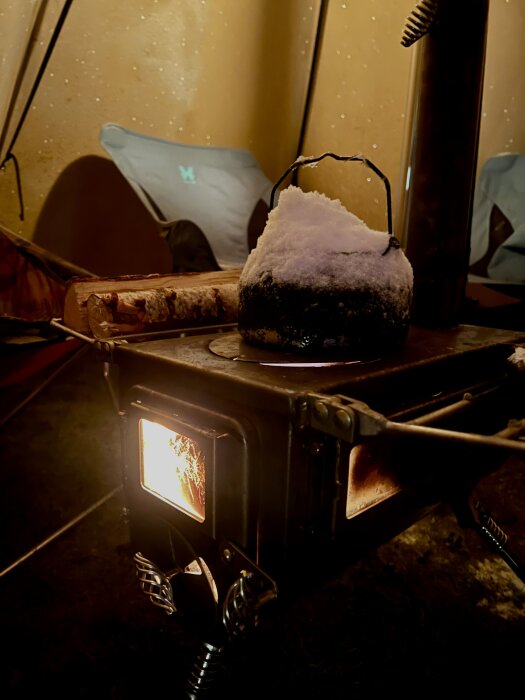 Inuti ett Tentipi Zirkon-tält med snötäckt kittel på en Winnerfell Woodlander-kamin, bakgrund av tältväggar och en stol.