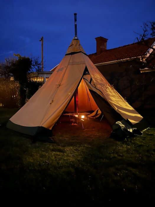 Tält i en trädgård kvällstid med öppen ingång som visar en liten kamin inuti.