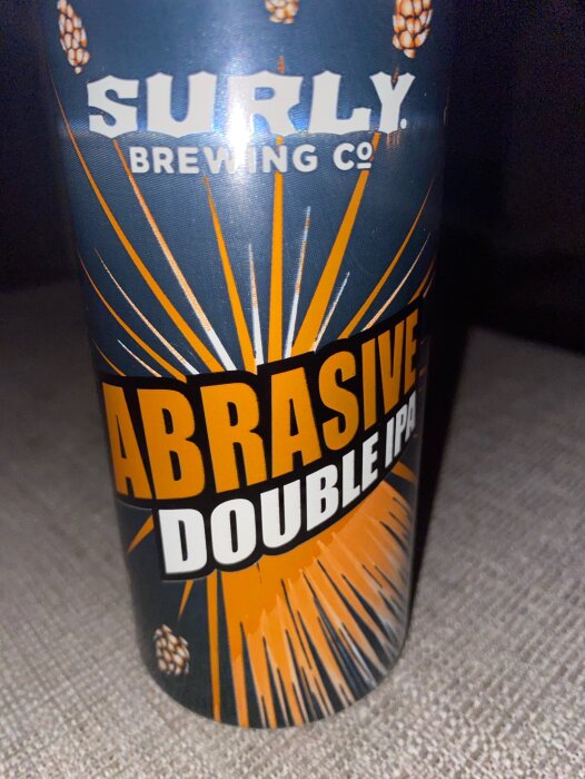 Burk av Surly Brewing Co. med etikett "Abrasive Double IPA". Design med orange och vit text samt humlekottar mot mörk bakgrund.