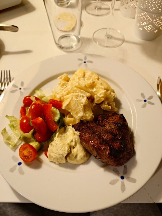 Tallrik med grillat kött, potatisgratäng, sallad och sås.