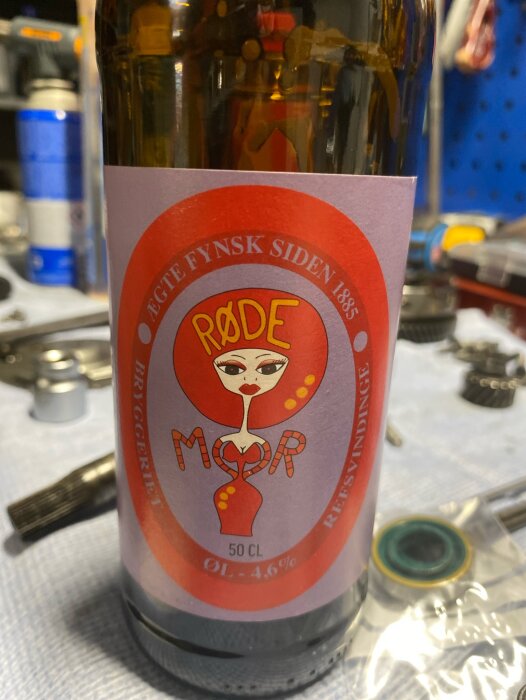 Flaska med etikett "Røde Mor" från Thisted Bryghus, 50 cl, 4.6% alkohol. Verktyg och bänkskiva syns i bakgrunden.