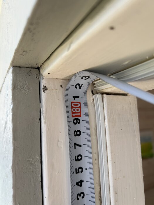 Måttband visar höjden på ett dörrhål i ett äldre dörrkarm. Mätvärdet visas tydligt, relaterat till byte av dörr och karm i en friggebod.