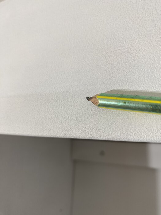 Närbild av en yta målad med grundfärg, visar ojämn struktur, med en penna som pekar på ytan.